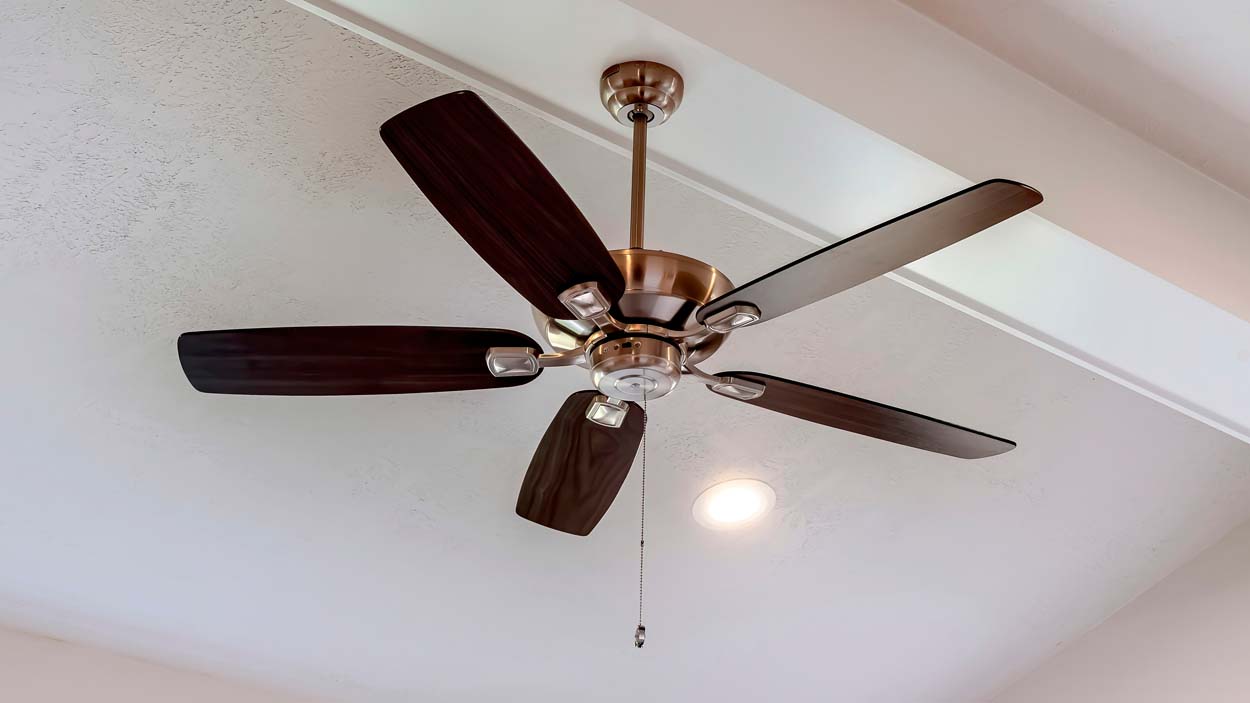 Panorama Decorative wood beam with standard ceiling fan and lights inside a house. Bright recessed round lights are also intalled on the white ceiling.